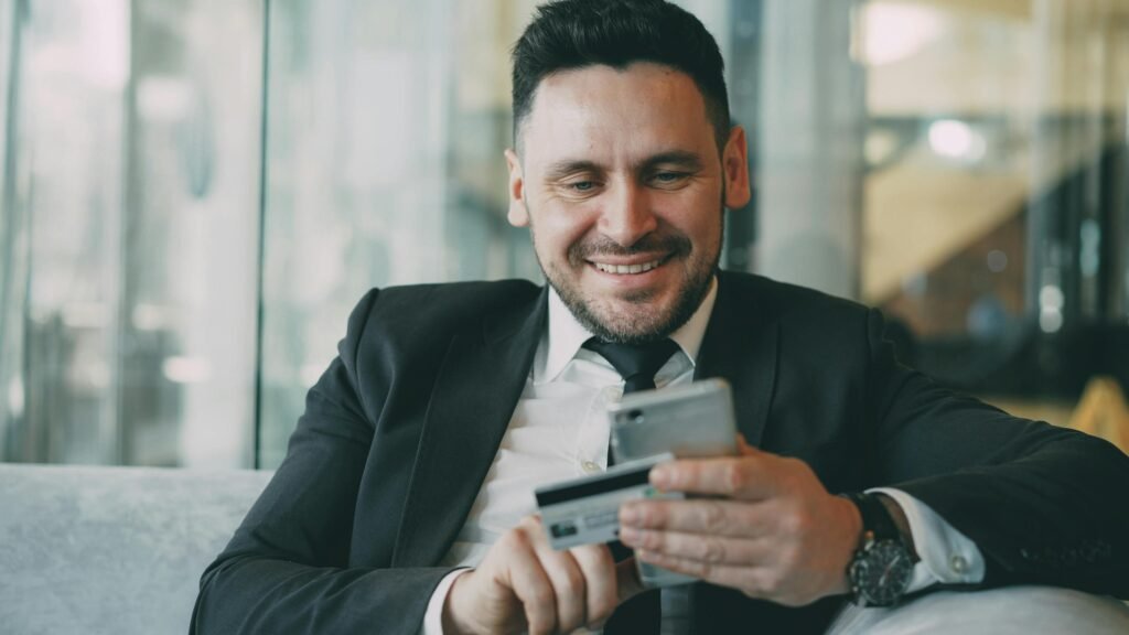 Smiling businessman using a smartphone and credit card for online shopping in a modern office.