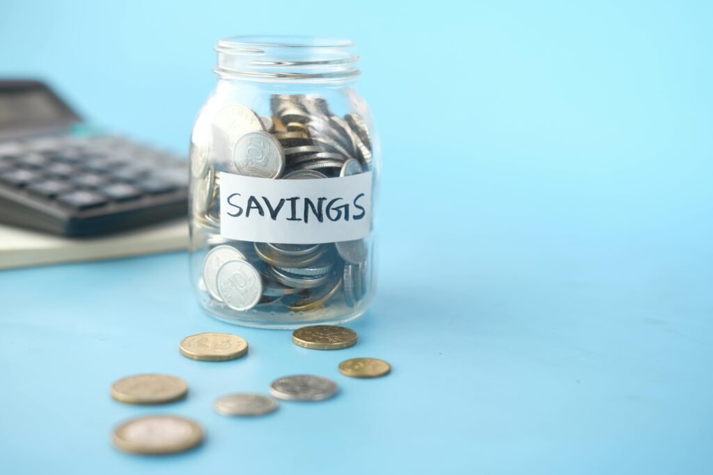 Glass jar labeled 'Savings' filled with coins, beside a calculator on a blue background.
