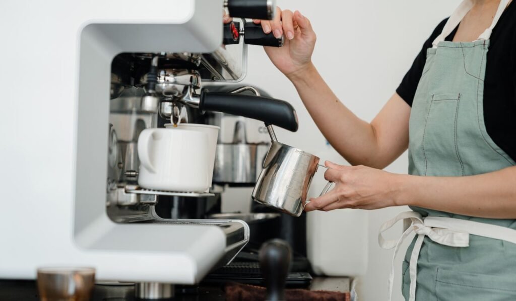 Barista steaming milk for a cappuccino behind the counter of a coffee shop