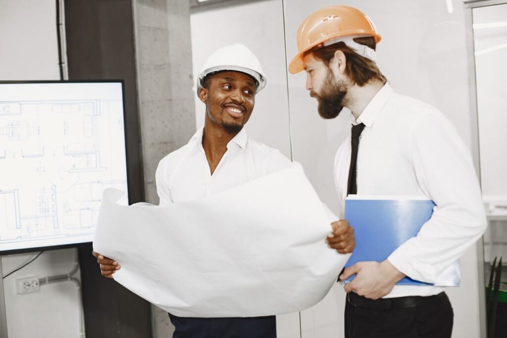 Two contractors in hard hats discussing blueprints in an office