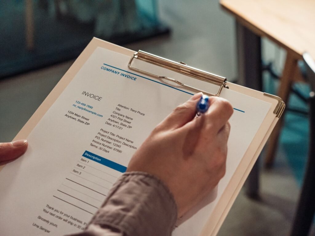 Hand holding a company invoice on a clipboard with a pen, ready to be completed at a desk