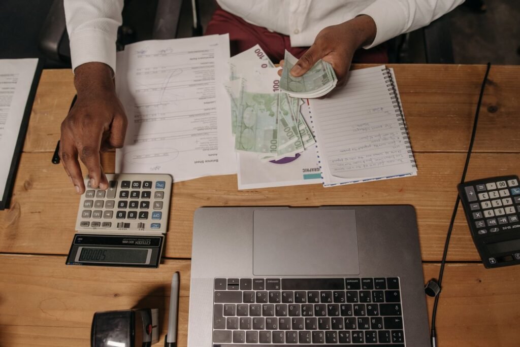 Small business owner counting cash with a calculator and financial documents at a desk