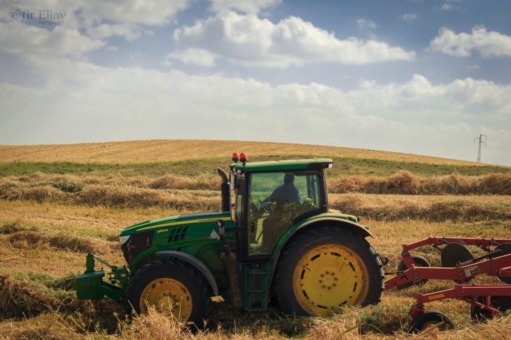 Green tractor working a hay field on a farm under blue skies